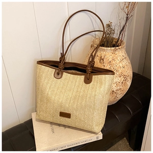 Detail of woven straw tote bag featuring brown leather handles and brand logo patch