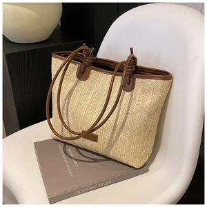 Detail of hand-woven beige straw tote with dark brown leather handles and knot accents