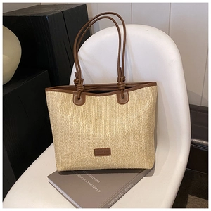Detail of woven straw tote bag with brown leather handles on a minimalist white chair