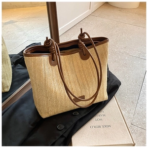 Close-up of a woven straw tote with dark brown faux leather handles and knotted strap detail