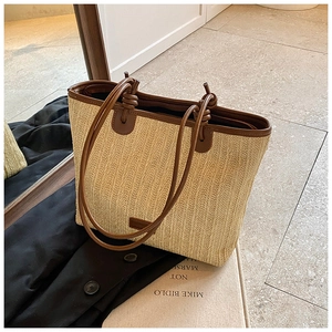 Detail of beige woven straw tote with brown leather handles and decorative knot accents