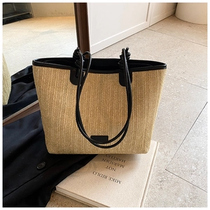Close-up of woven straw tote bag with black leather shoulder straps on art book