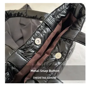 Detail of silver magnetic snap closures on a black quilted puffer tote bag