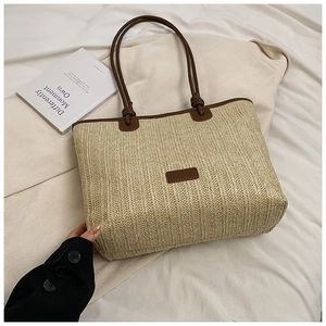Detail of woven straw tote bag with brown leather handles on white wrinkled background