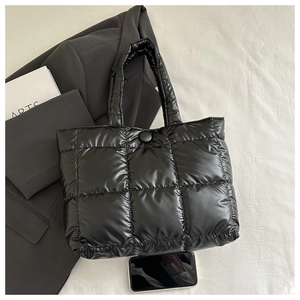 Detailed view of black quilted tote bag with smartphone for size comparison