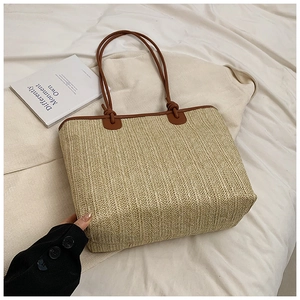 Close-up of woven straw tote bag with brown leather handles on a white fabric background