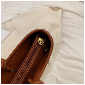 Detail of golden metal zipper and smooth brown leather stitching on the woven tote bag