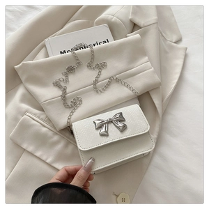 Close-up of white snake pattern crossbody bag with silver metal bow and chain strap
