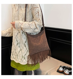 Brown suede crossbody bag with long tassels shown on a model in a minimalist setting