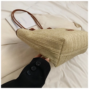 Close-up of woven straw tote bag with brown leather straps on a soft fabric surface