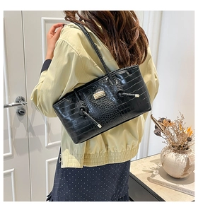 Detail of black crocodile texture shoulder bag with gold logo and side drawstring accent