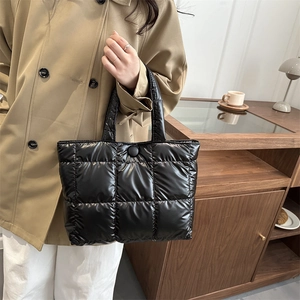Quilted black tote bag with glossy finish and snap button held by a person in a trench coat