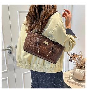 Detailed view of dark brown crocodile embossed leather tote with elegant gold logo plate
