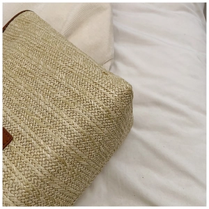 Detail of woven straw bag showing fine twill texture and brown leather corner accent