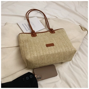 Close-up of beige straw tote bag with brown leather handles and textured weaving