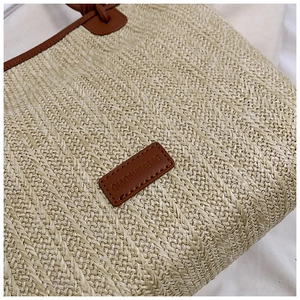 Detailed view of woven straw tote bag texture and brown leather brand label