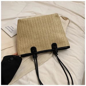 Detail of handwoven straw tote with black faux leather trim and vertical texture