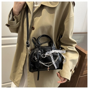 Detail of black glossy PU leather baguette bag with lace bows and cross pendant on model