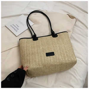 Close-up of woven straw tote bag with black leather straps and brand patch detail
