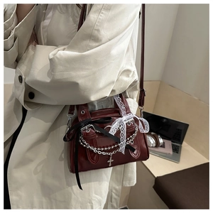 Close-up of wine red glossy handbag featuring silver chains, lace bows, and cross charms