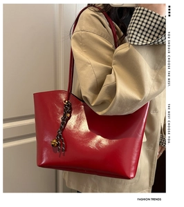 Detail of red wax leather tote bag featuring braided strap and metal bell charm