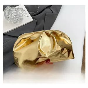Detailed close-up of a gold metallic cloud clutch with luxury pleated texture on grey fabric