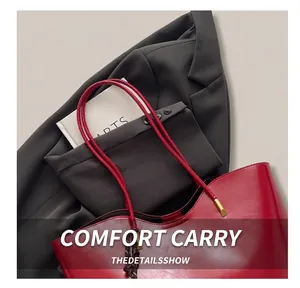 Detail of red leather tote bag showing slim handles and metallic hardware on a minimalist suit