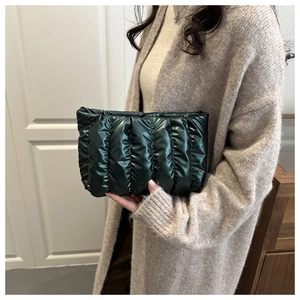 Detail of dark green quilted clutch with wavy folds and glossy metallic finish