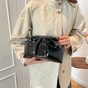 Minimalist black pleated cloud clutch bag with glossy finish held by a model