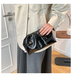 Detail of elegant black pleated evening clutch bag held against minimalist home background