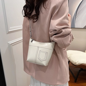 Minimalistische beige Crossbody-Beuteltasche mit Schilddeko am Model zu Hause