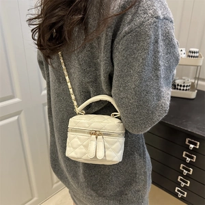 Ivory quilted mini box bag with gold chain strap shown on model in a modern interior