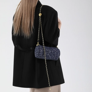 Sac cylindre en tweed bleu marine avec chaîne dorée, porté par un mannequin pour le style