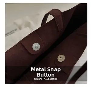 Detail showing the silver magnetic snap closure on a dark brown suede tote bag