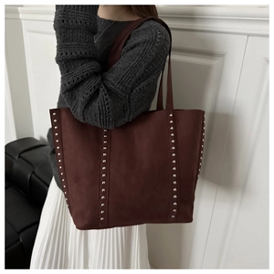 Detail of burgundy matte leather tote bag with silver studs worn by a model in winter