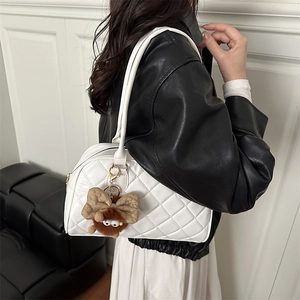 White quilted tote bag with brown plush monster charm shown on model in stylish setting