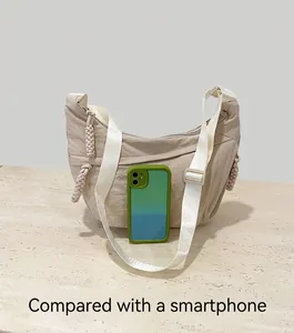 Detailed comparison of the beige nylon crescent bag size with a mobile phone on a stone surface