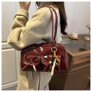 Detail of wine red glossy shoulder bag with bow pockets and wooden bead charm accessory