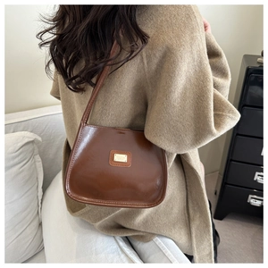 Detail view of a vintage brown leather underarm bag worn on the shoulder in a home setting