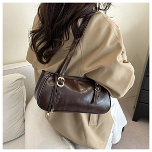 Detail of dark brown glossy leather baguette bag with dual golden buckles on shoulder strap