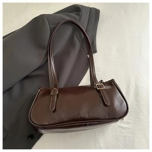 Close-up of glossy brown faux leather underarm bag with gold metal buckles and stitching