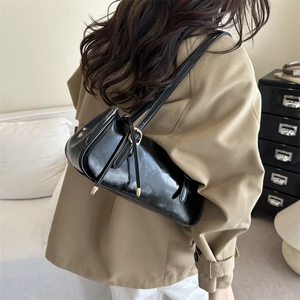 Glossy black baguette shoulder bag with metallic buckle shown in a side view on a model