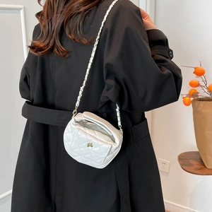 White quilted crossbody bag with gold camellia clasp and chain strap on a black coat
