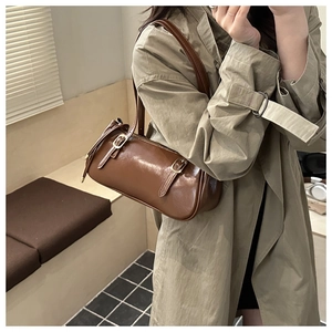 Close-up of a vintage brown cylindrical leather baguette bag with gold buckle straps