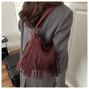 Detail of burgundy fringe crossbody bag with suede texture and gold hardware rings