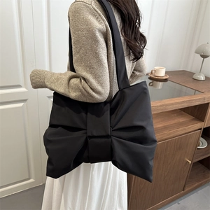 Minimalist black nylon tote bag with large decorative bow design shown on shoulder