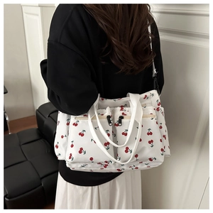 Detail of white corduroy bag with red cherry prints and three front zip pockets