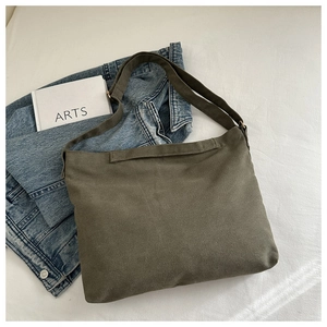 Flat lay of large olive green canvas messenger bag on white fabric with books
