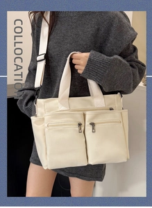 Detail view of a cream canvas tote bag with dual front zipper pockets and wide strap