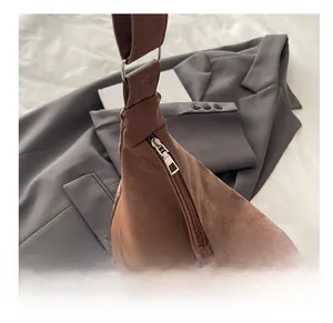 Detail of smooth metal zipper on minimalist brown suede shoulder bag with soft pleats